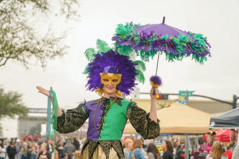 Lady dressed in full Mardi Gras outfit with decorated umbrella at a festival.